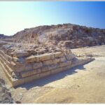Ruins of the Djedefre Pyramid with weathered stone blocks under a clear blue sky.