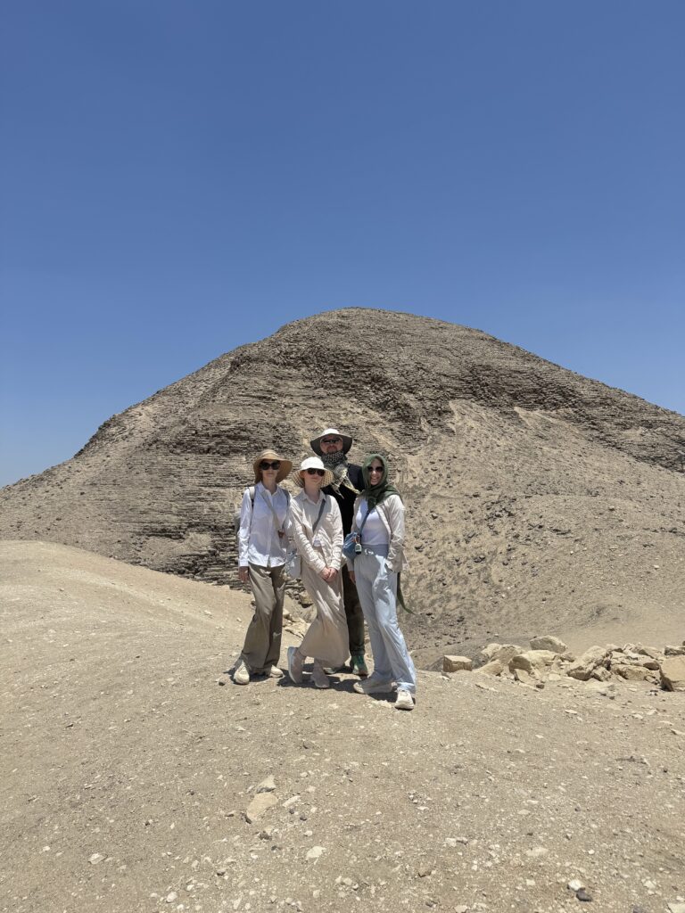 Four visitors pose in front of the Pyramid of Nyuserre at Abusir, surrounded by desert.