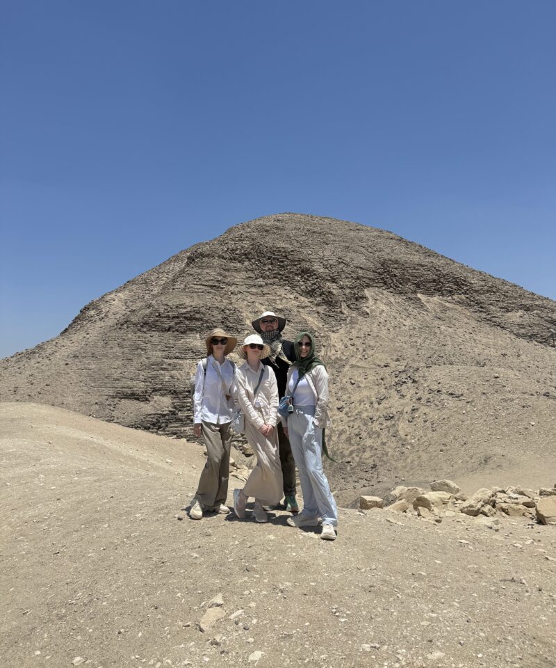 Four visitors pose in front of the Pyramid of Nyuserre at Abusir, surrounded by desert.
